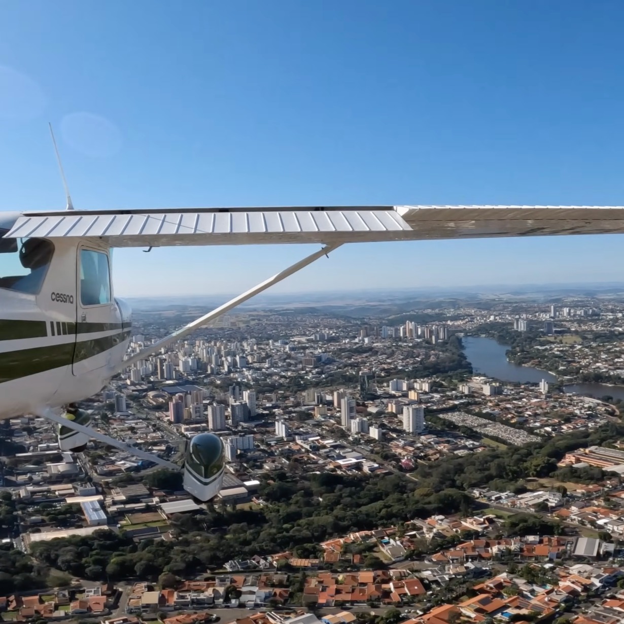 A city and river seen from the air, with the wing of a small airplane in the foreground.