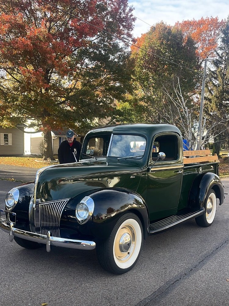 A dark green vintage pickup truck on a street beneath autumn trees.