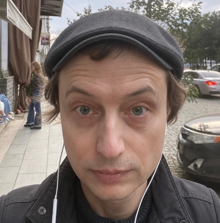 Denis Ostapenko outdoors, wearing a gray cap and earphones.