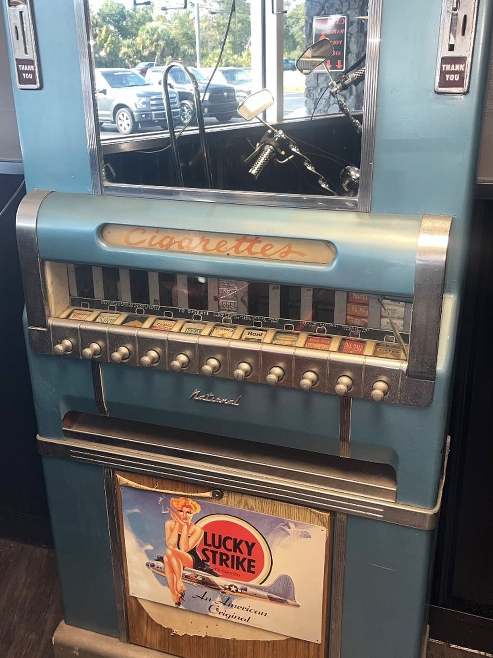 An old blue cigarette vending machine with metal pull knobs and a mirror.